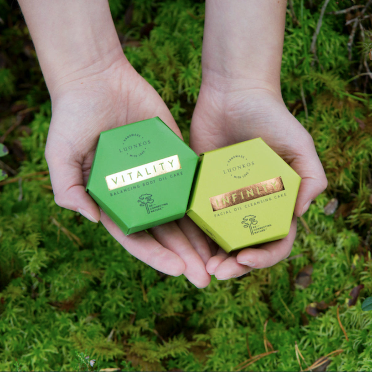 Fragrance-free oil cleansing cakes by Luonkos, featuring Infinity and Vitality, held in hands over moss.